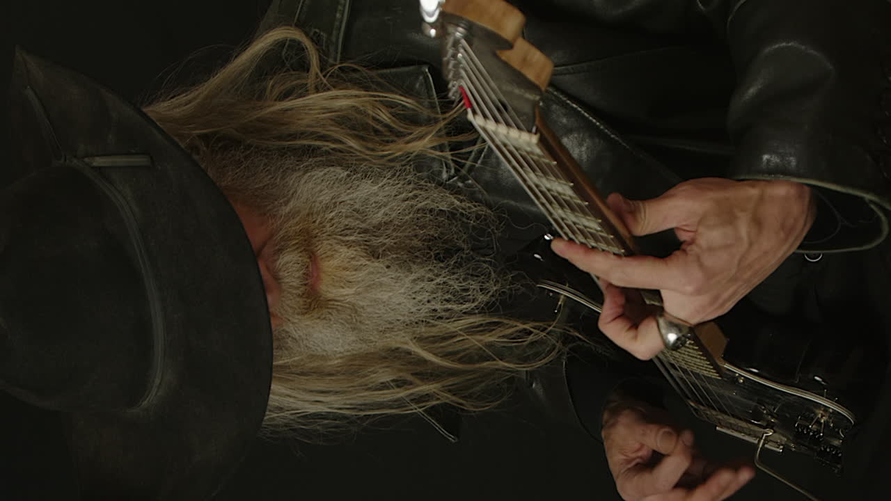 Vertical format: Bearded man in black Stetson plays electric guitar