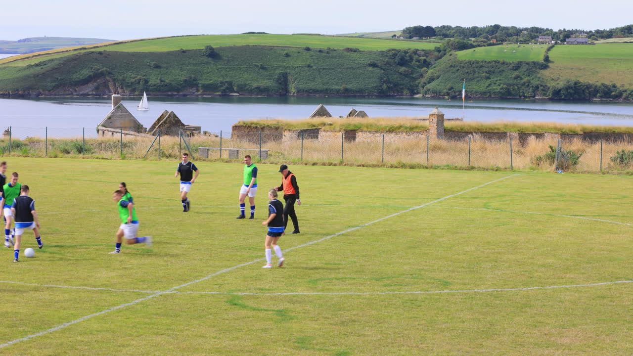 Male and female soccer players playing soccer, passing and running after ball with coach on pitch