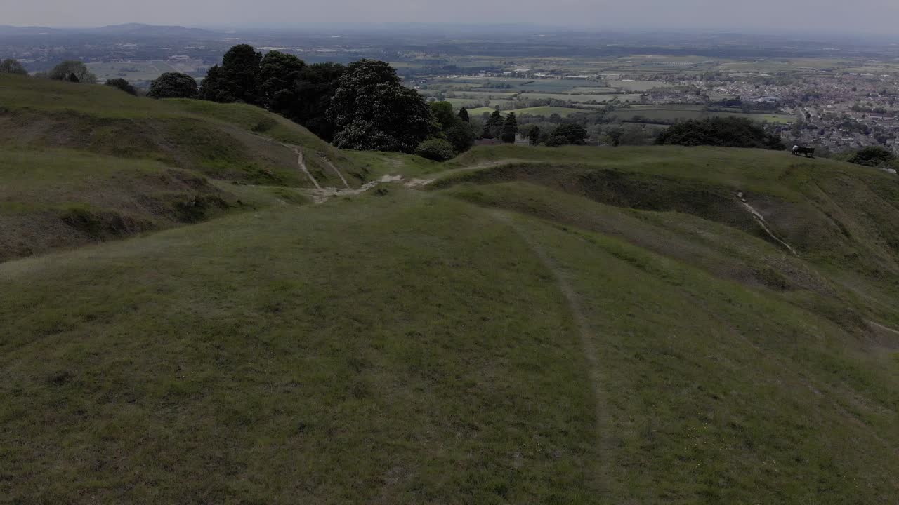 Drone shot of The Cotswolds. Drone fires up in the sky quickly to reveal a wide shot of a small town and the surrounding nature.