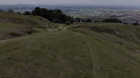 Drone shot of The Cotswolds. Drone fires up in the sky quickly to reveal a wide shot of a small town and the surrounding nature.