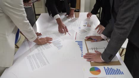 recortado con vista de cerca manos de un equipo de negocios de lluvia de ideas juntos haciendo planes de inversión con papeles y estadísticas en la mesa en el lugar de trabajo