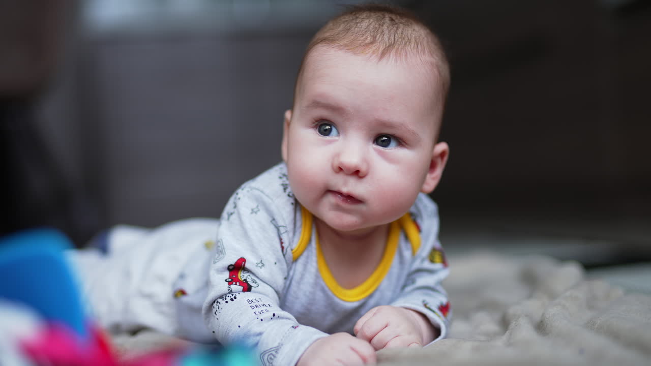 Cute adorable baby boy lies on tummy looking aside. Lovely beautiful kid smiling sweetly to something. Close up.