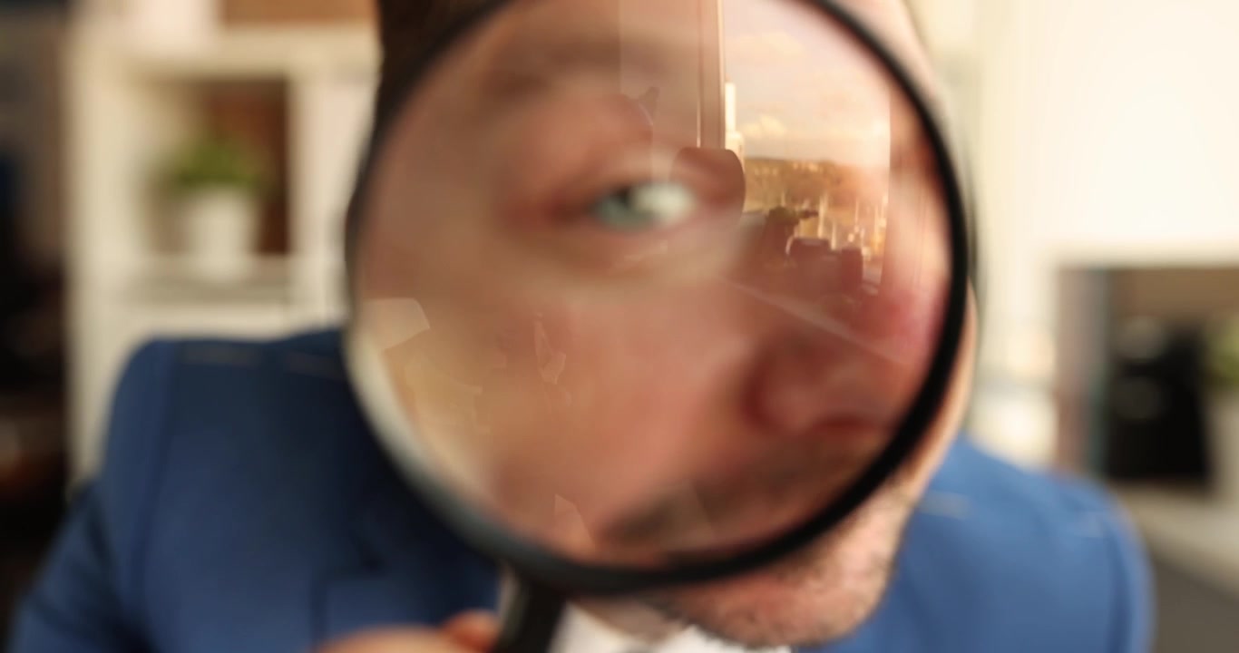 Smiling businessman looks through magnifying glass to camera