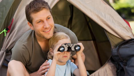 smiling caucasian father and child in tent, child birdwatching with binoculars