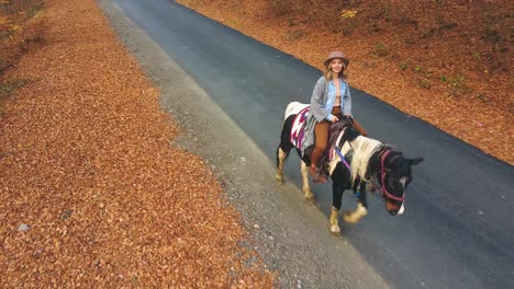 niña montando un caballo en un camino rural con hojas de naranja en el suelo