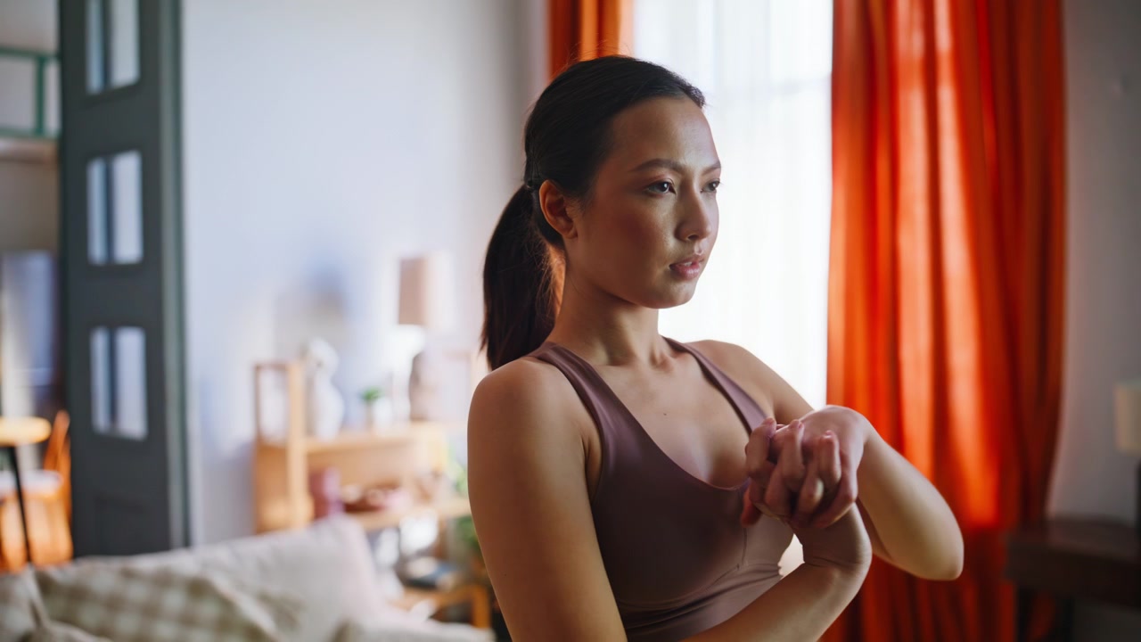 Donna asiatica che allunga polsi e braccia prima dell'allenamento a casa. Primo piano di riscaldamento fitness.