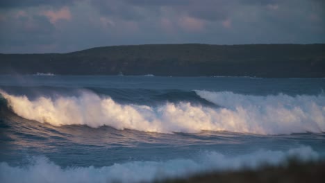 ocean waves roll into a coastline in golden light in slow motion