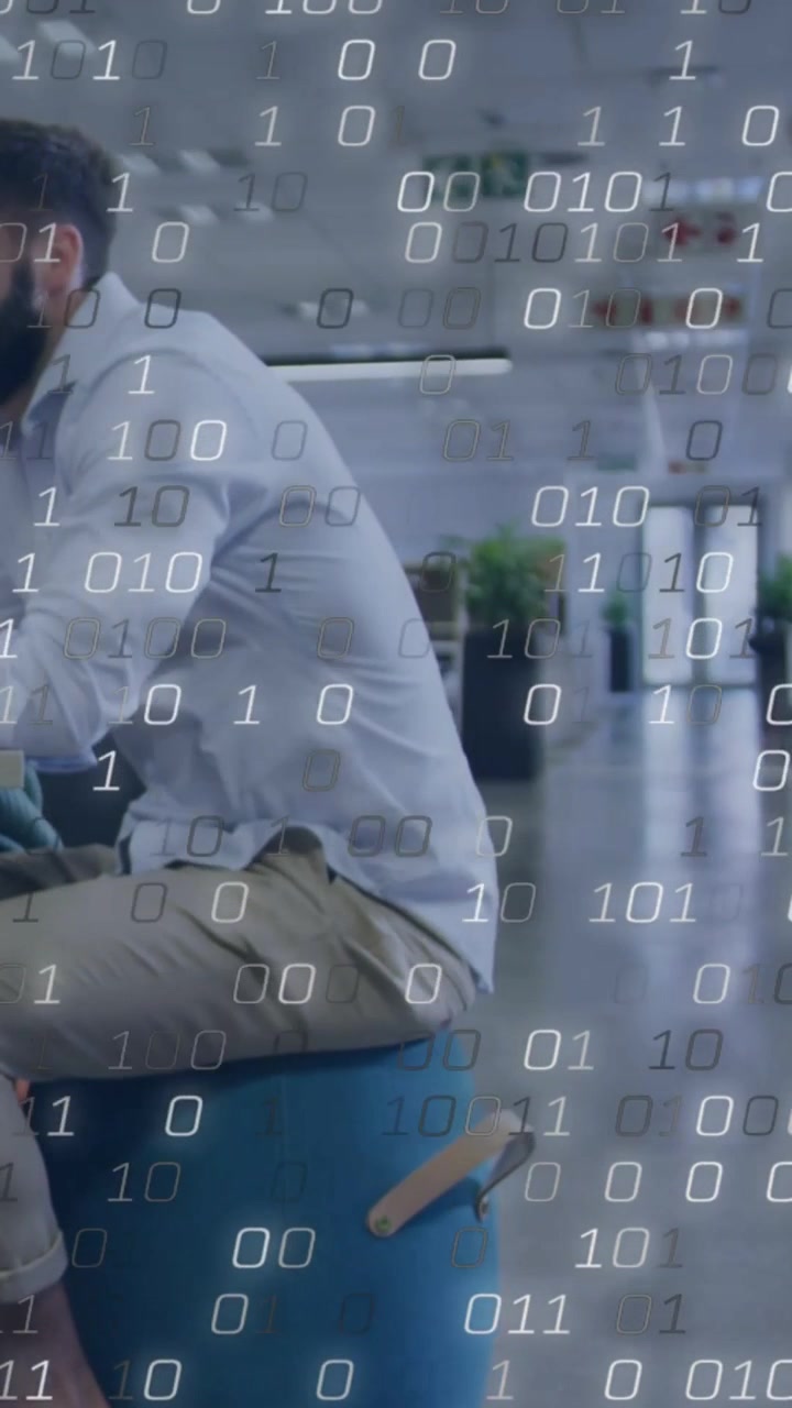 Vertikales Video: Arbeitender Mann in Hemd und Khakihose auf blauem Hocker im Büro, aufsteigender Binärcode, Platz für Text.