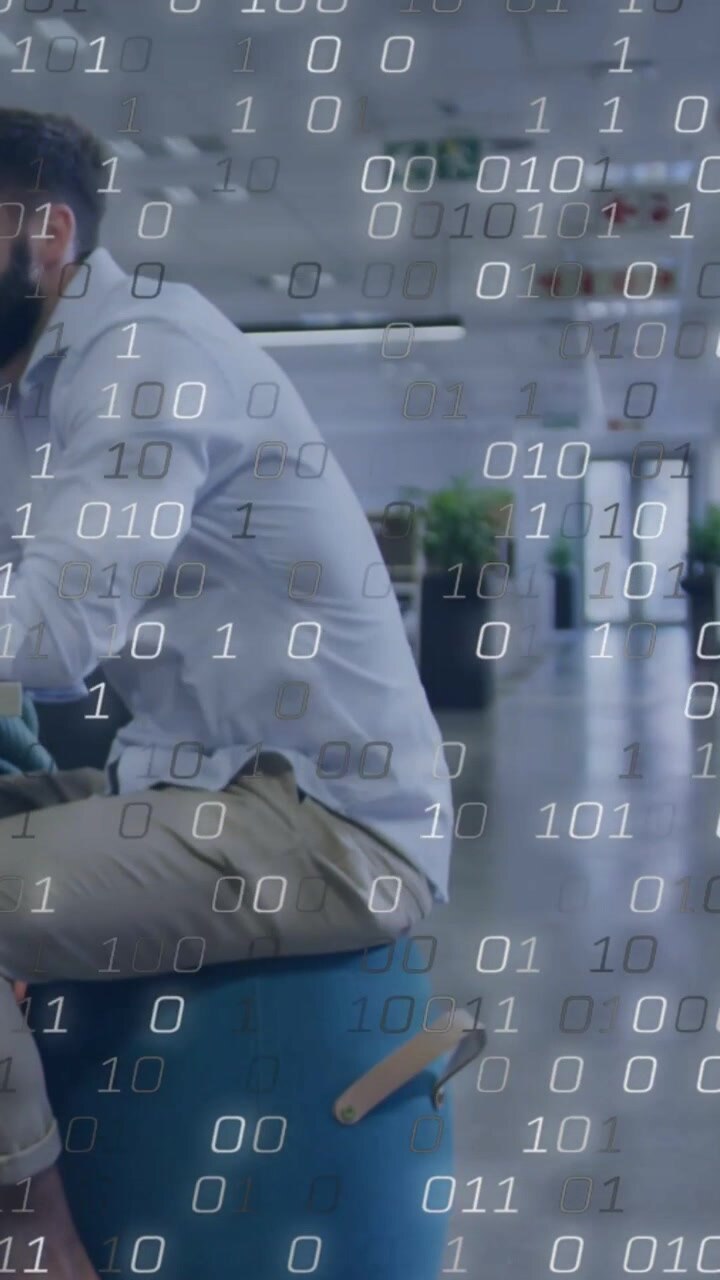 Vertikales Video: Arbeitender Mann in Hemd und Khakihose auf blauem Hocker im Büro, aufsteigender Binärcode, Platz für Text.