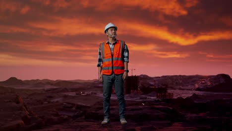 cuerpo lleno de ingeniero masculino asiático con casco de seguridad mirando a su alrededor mientras está de pie en el sitio de construcción, maquinaria de minería