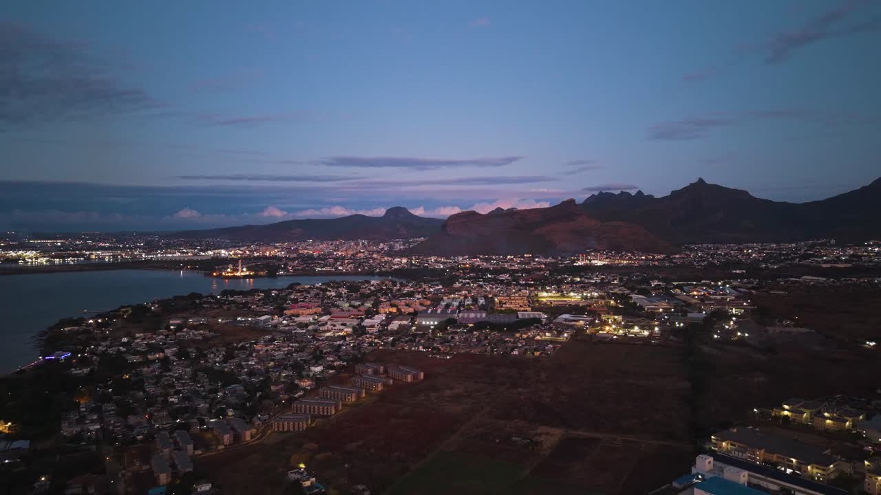 Aerial sunset view of Port Louis, Mauritius, showing city lights, harbor, and surrounding mountains as daylight fades into dusk under a clear tropical sky