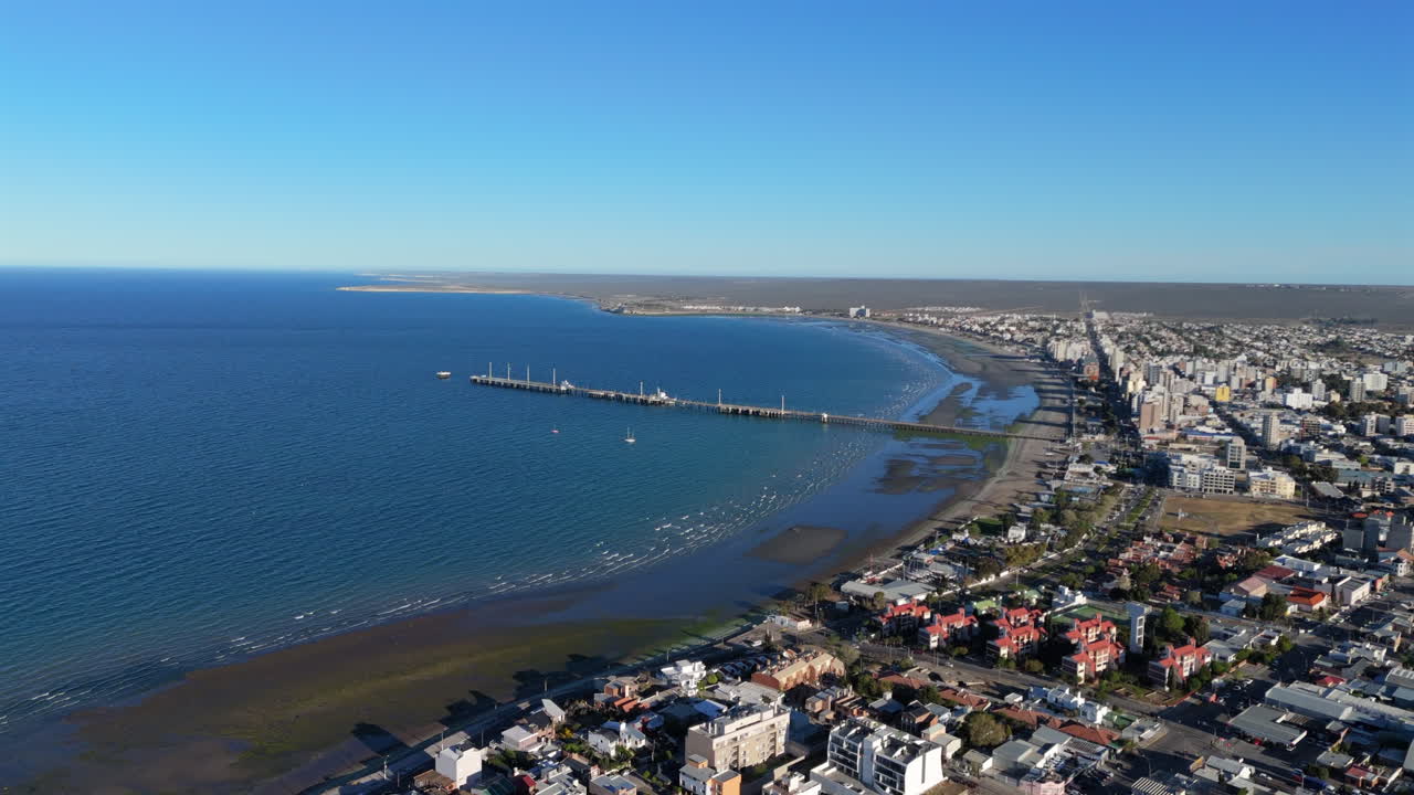Panorama drone view of the Muelle Comandante Luis Piedra Buena pier and coastal town with blue ocean, Patagonia Chubut, Puerto Madryn, Argentina.