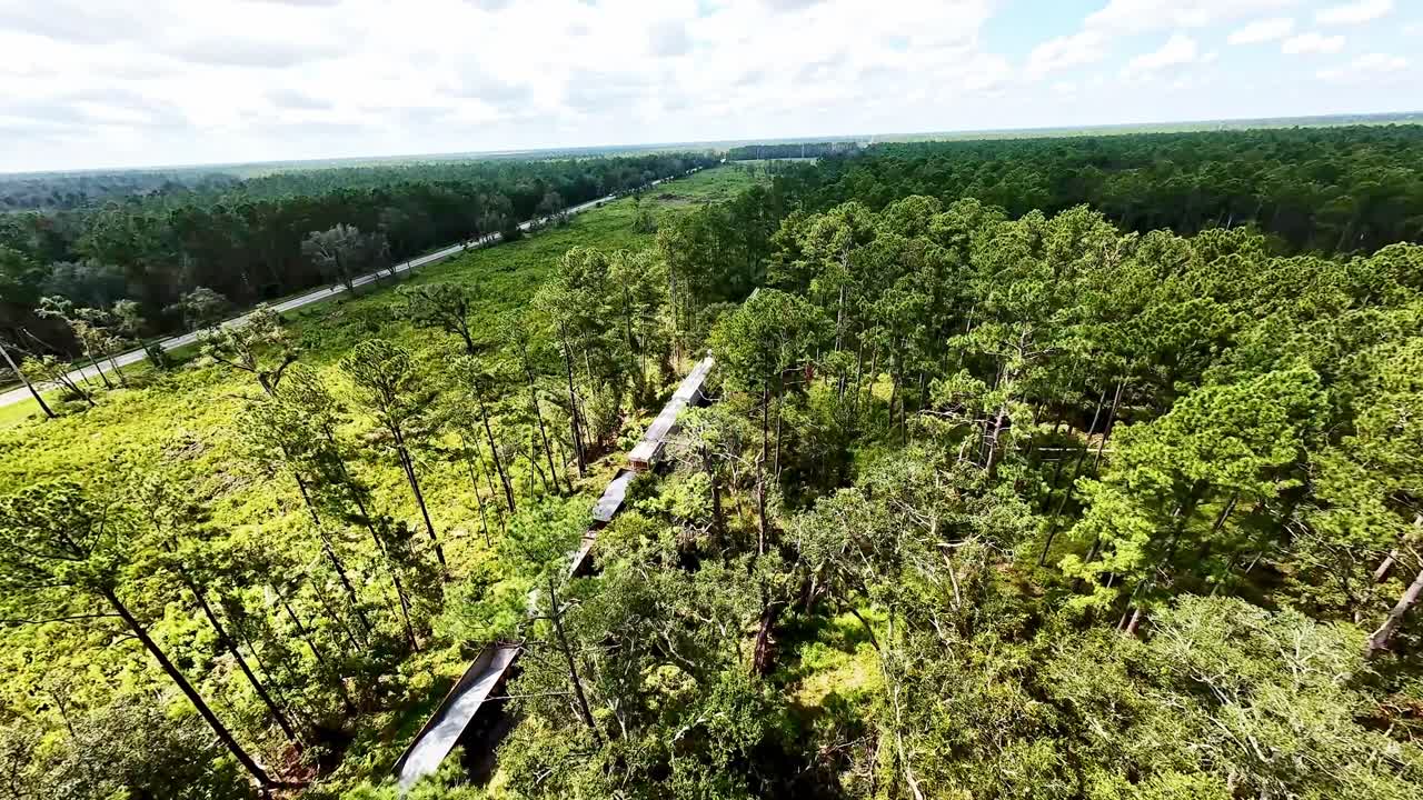 Low aerial footage tracking a freight train traveling along the Florida Central and Western Railroad near Ellaville, showcasing lush green surroundings and local scenery.