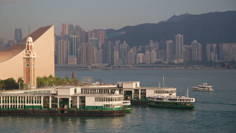 enjoy a captivating view of kowloon ferry terminal and clock tower in hong kong, featuring ferry boats and the stunning skyline as the sun sets, casting beautiful colors over the water and cityscape