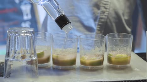 barman pouring alcohol into four cups in a bar