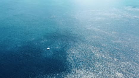 aerial distant view of sailboat looking very small in a vast blue ocean with some clouds overhead in south pacific ocean