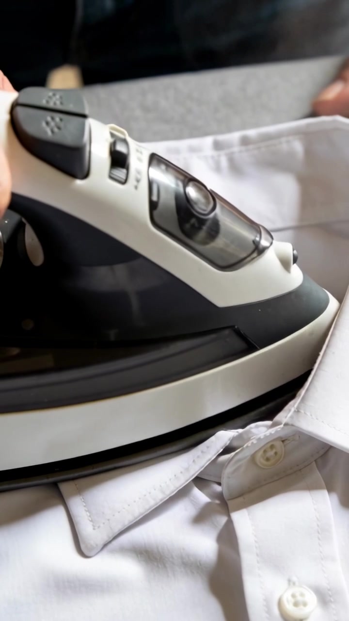 Vertical video: Pressing steam iron on collar, adult smoothing white shirt at home removing creases