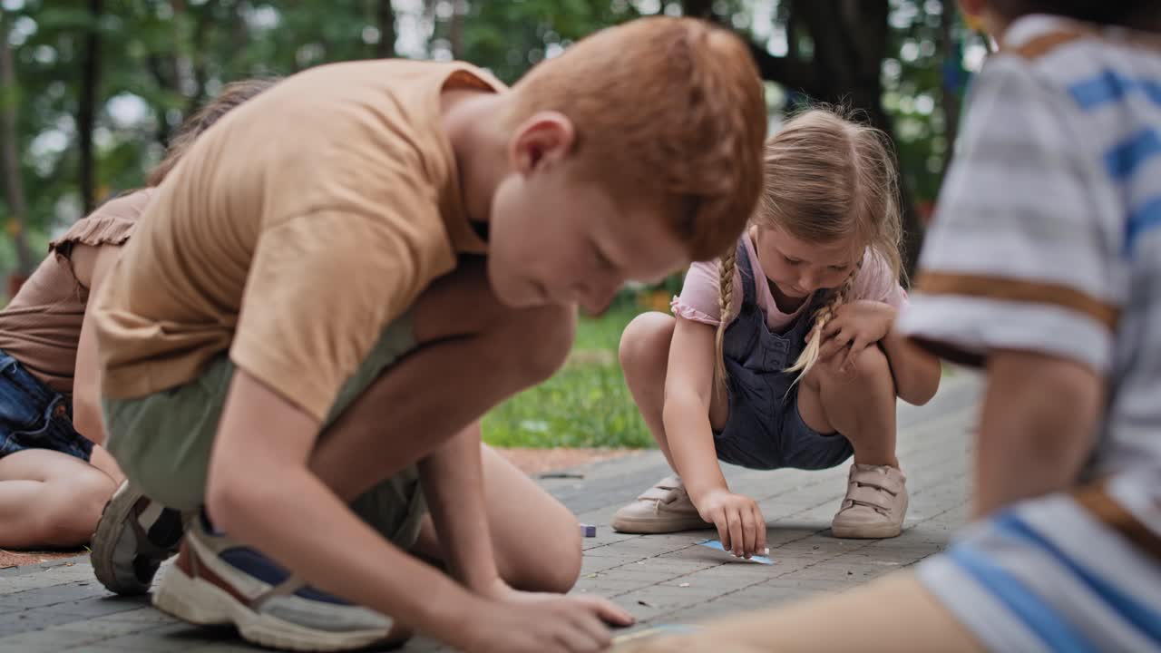 grupo de niños caucásicos coloreando con tiza en un día de verano en el parque.