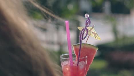 mujer de vidrio con cóctel refrescante contra las palmas borrosas