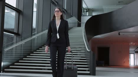 mujer de negocios con un traje de negocios con una maleta camina por el aeropuerto o el centro de negocios y habla por teléfono. una mujer europea confiada