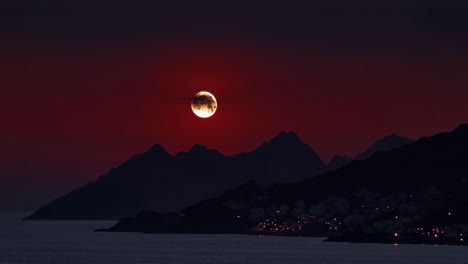 dramatic blood moon over coastal mountains and town at night
