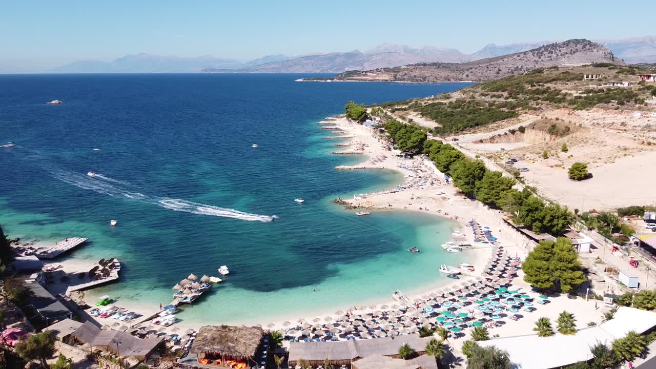 Aerial Drone View of Ksamil Beach, Ionian Sea, Albania - Sunbeds, Jetski, Hotels and clear blue sea