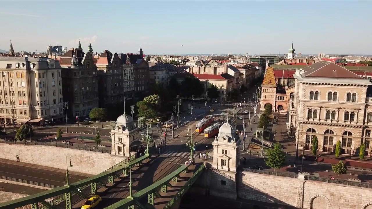Veduta aerea del Ponte della Libertà, un ponte in acciaio verde sul fiume Danubio, con un tram e auto che passano e lo skyline di Budapest sullo sfondo durante una giornata di sole, Ungheria, ripresa aerea con drone.