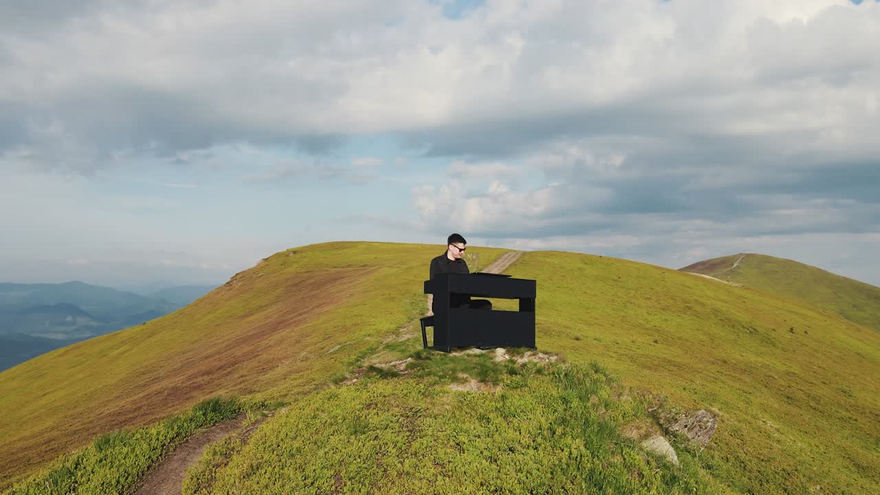 피아니스트가 산에서 그랜드 피아노를 연주하는 공중 풍경: 두 손의 남자가 자연에서 그랜드피아노에서 부드러운 클래식 음악을 연주합니다.