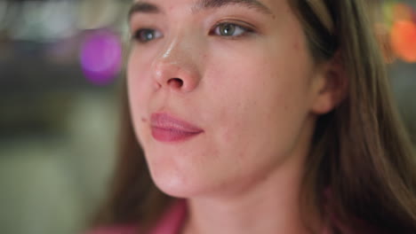 close-up of a woman licking her pink lips as if she has something in her mouth spots are seen on her face, with colored blurred lights blinking in the background, and unclear object in behind her