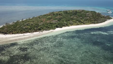 Drone-aerial-moving-backwards-slowly-to-reveal-green-forest-tropical-island-the-blue-clear-reef-ocean