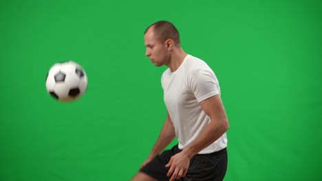 Concentrated inspired Caucasian football player catching ball with chest juggling with legs in slow motion leaving. Portrait of focused skilled sportsman playing soccer at chromakey background.