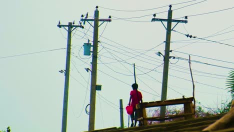 a boy in red shirt walks by electricity poles with a red bucket at dusk in coastal area of kuakata, bangladesh