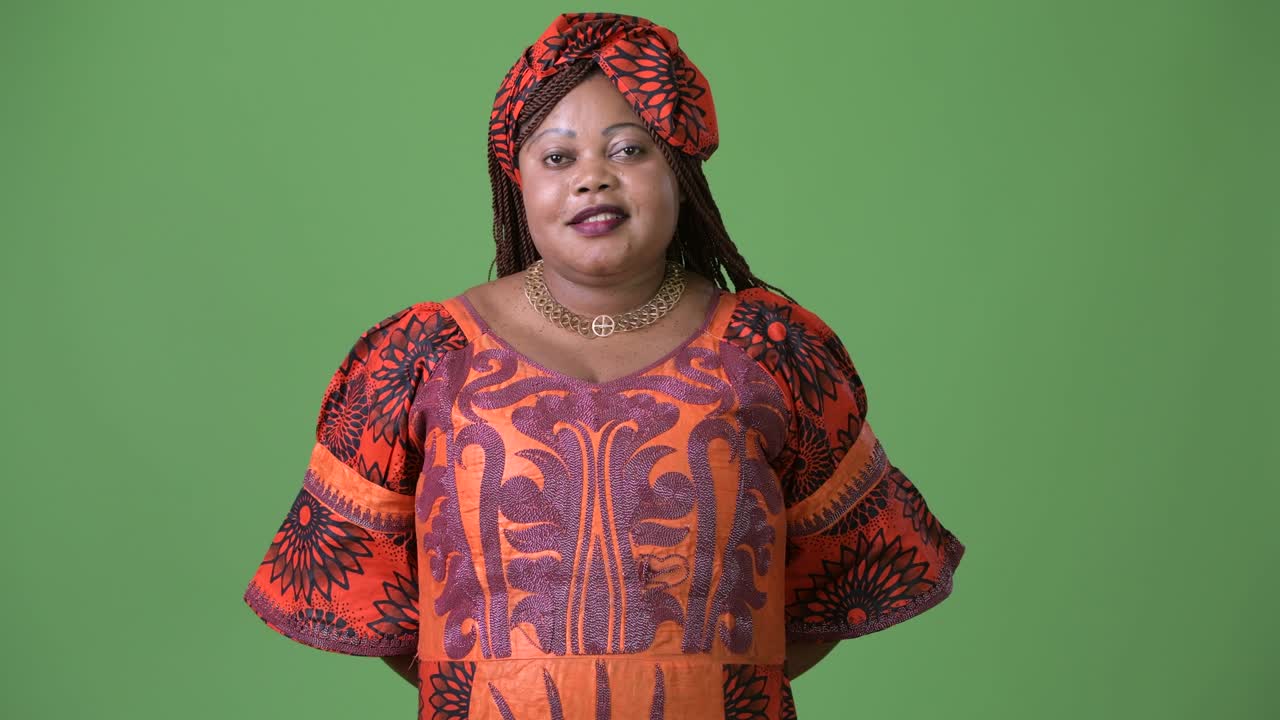 Overweight beautiful African woman wearing traditional clothing against green background