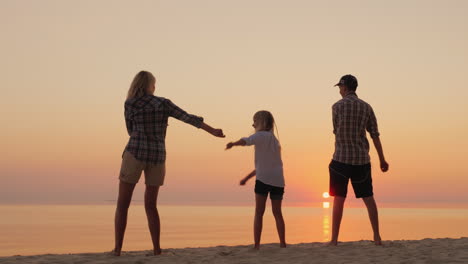 A-Young-Mother-With-Two-Children-Is-Teaching-A-Fashionable-Dance-Movement-On-The-Beach-At-Sunset-Com