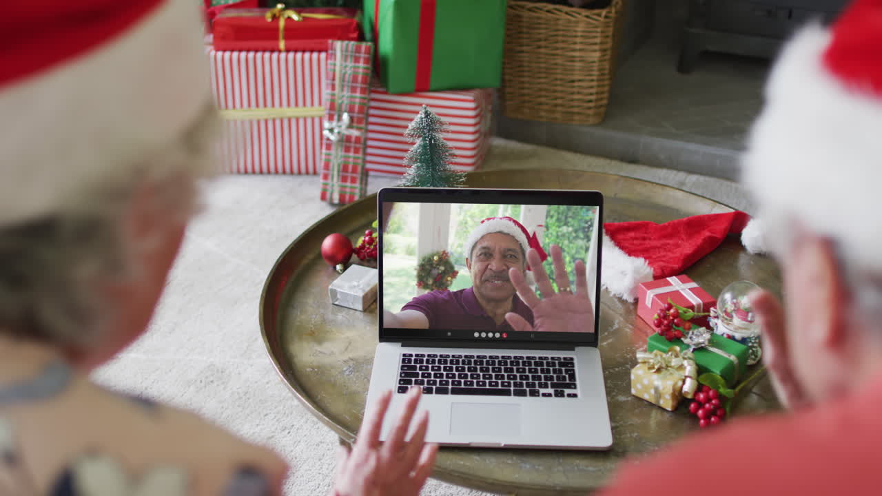 pareja de alto nivel caucásica con sombreros de santa usando una computadora portátil para una videollamada de navidad con un hombre en la pantalla