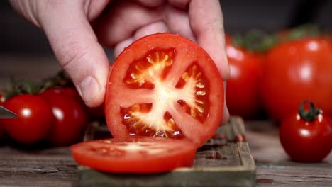 hand of a man with a knife cut a fresh tomato into pieces.