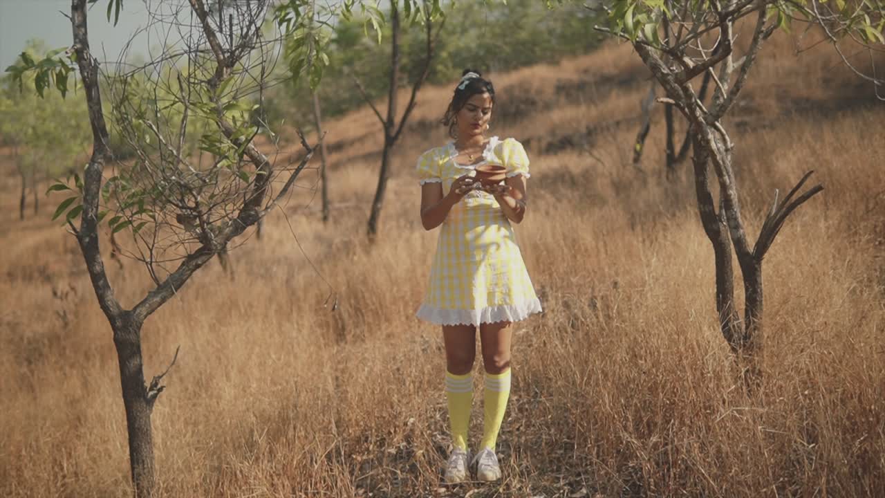 hermosa joven sosteniendo una olla de barro al aire libre en los campos con árboles prominentes que los rodean