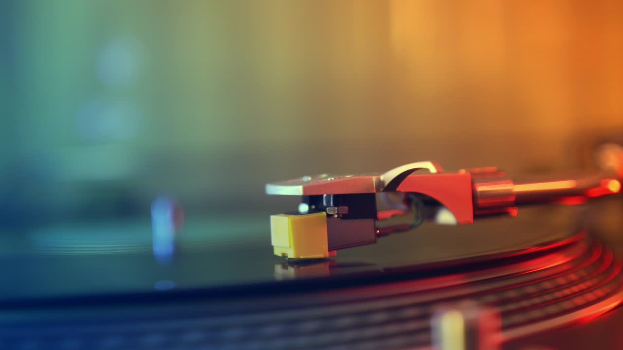 비닐 플레이어 턴테이블: 회전하는 비닐 레코드의 조각, 바늘을 클로즈업으로 가진 스타일러스, 바늘과 비닐 판을 멈추는, 매크로, 전면 뷰, 빨간색과 파란색 빛의 배경에서 흐릿한.
