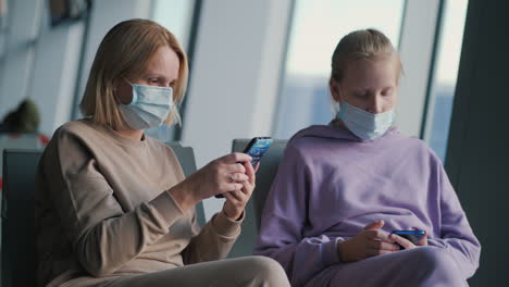 a parent with a child is waiting for a flight in the airport terminal. on the faces of protective masks, use smartphones