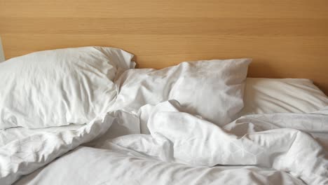 unmade bed with white bedding and wooden headboard