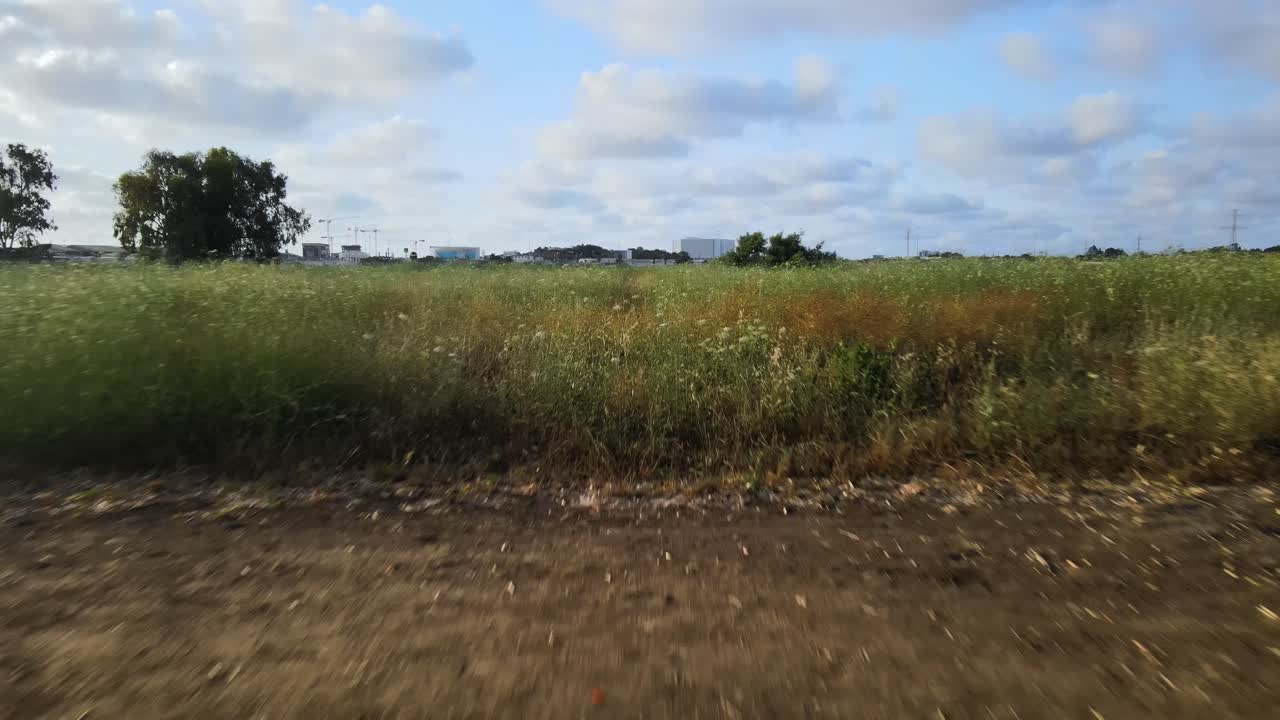 Un drone vola lungo un sentiero lasciando la linea degli alberi che si apre su un grande campo erboso.