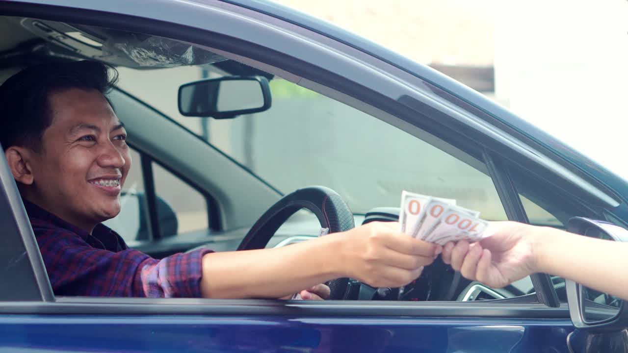 Cheerful Asian Man In Car Paying With Cash Through The Open Window