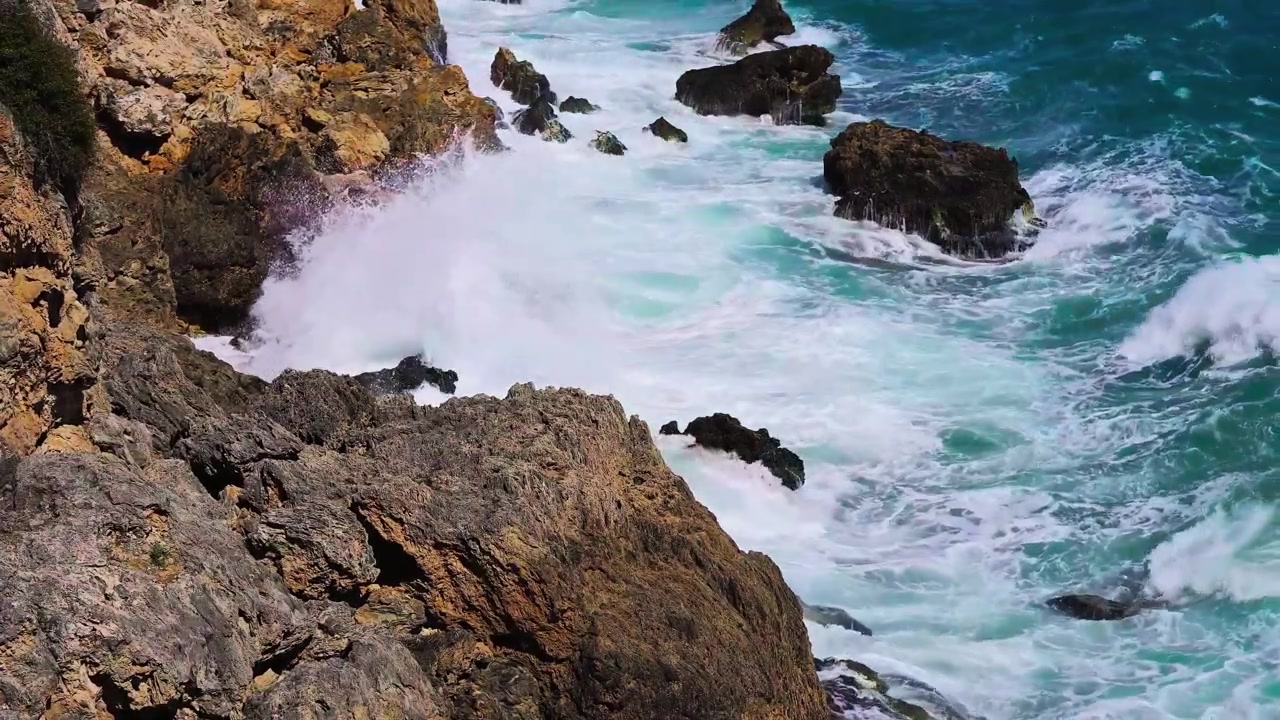 Una vista mozzafiato cinematografica dall'alto con carrellata che cattura enormi onde oceaniche spumeggianti che si infrangono violentemente su rocce vulcaniche nere affilate come rasoi.