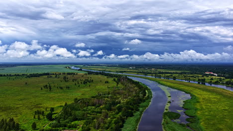 a beautiful aerial flyover shot soars above the winding lielupe river and its lush green banks near jelgava, latvia, under a dramatic sky filled with clouds