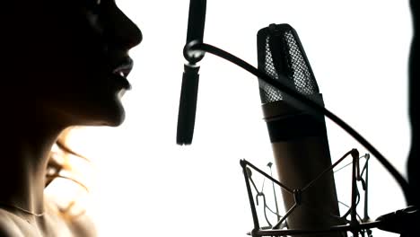 beautiful woman singing into a microphone in a recording studio.