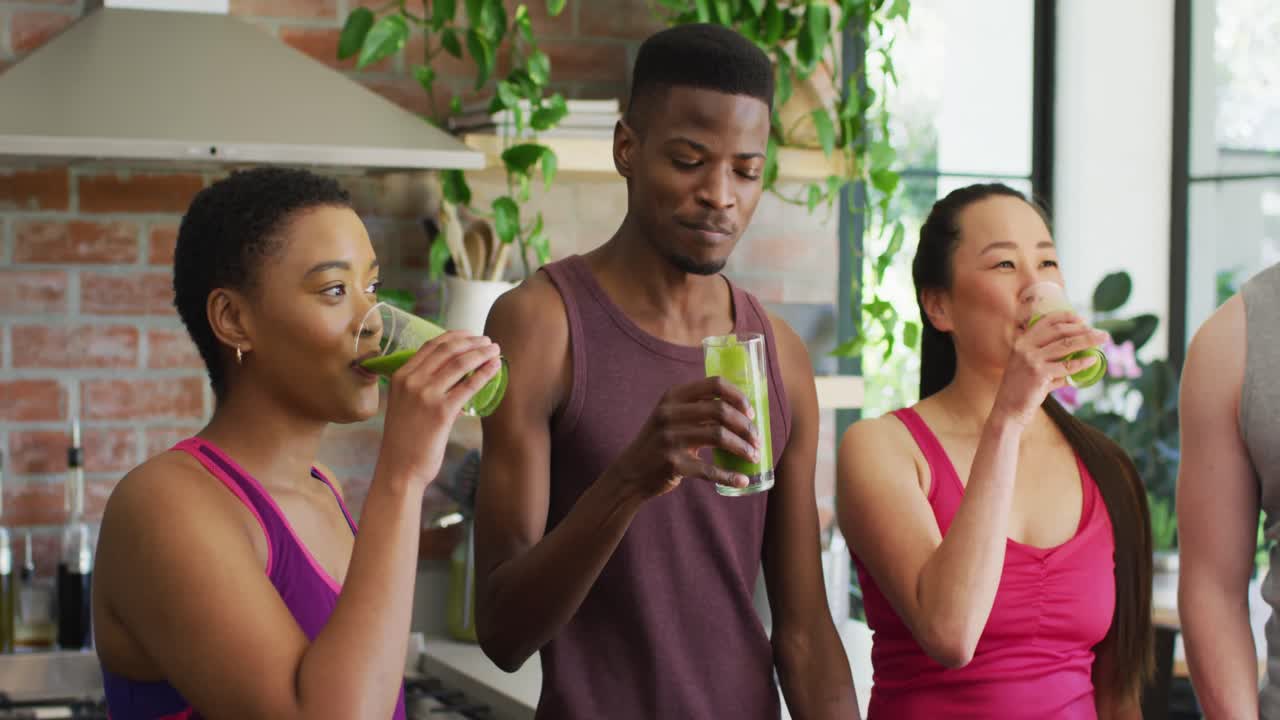 Groupe de jeunes diversifiés buvant ensemble un smoothie vert sain à la maison.