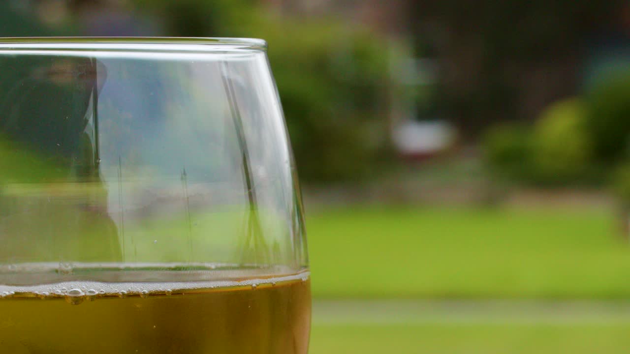 Golden beer pours into clear glass, forming bubbles and foam, with soft natural outdoor lighting