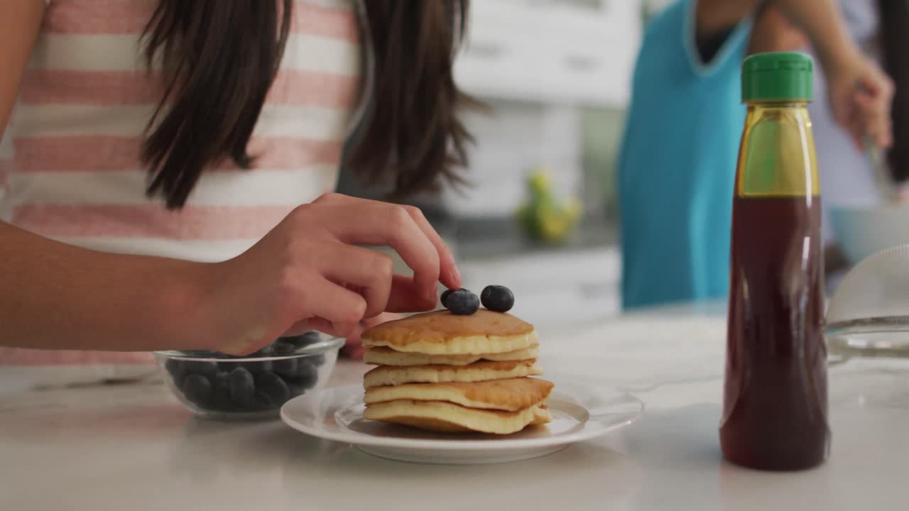 sección media de hermano y hermana en la cocina, hermana poniendo bayas en una pila de panqueques