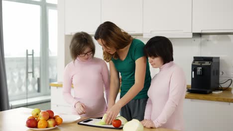 dos niñas con síndrome de down están aprendiendo a cocinar con su madre en la cocina en casa con diversión y sonrisa