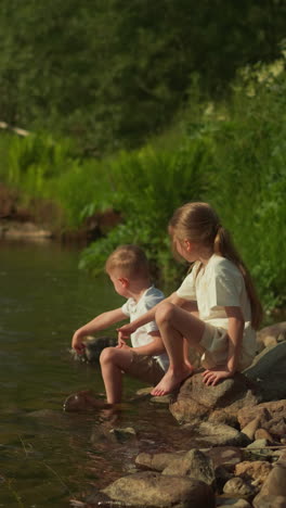 girl and boy throw stones into river playing together in nature. spending summer holidays with family in tourist place without using gadgets for children slow motion